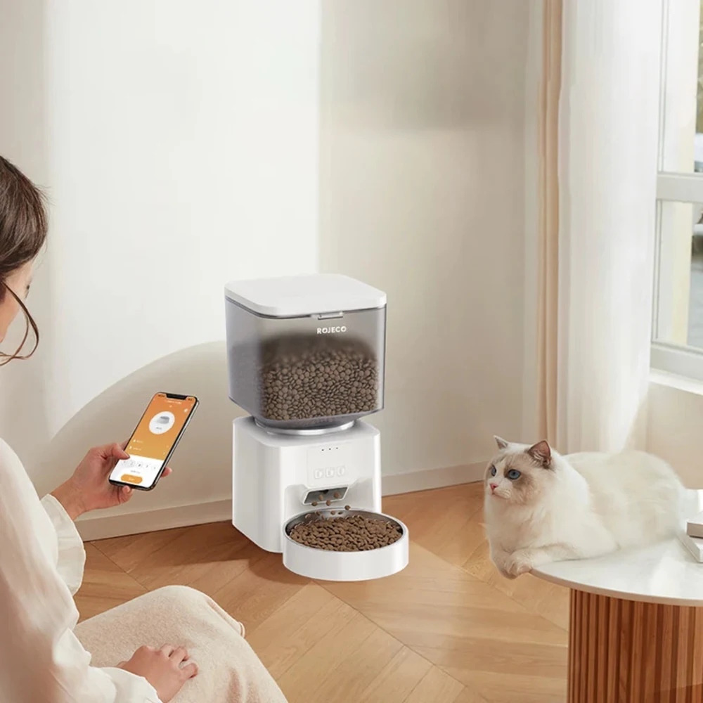 Femme contrôlant un nourrisseur automatique Rojeco via smartphone, chat blanc assis à proximité