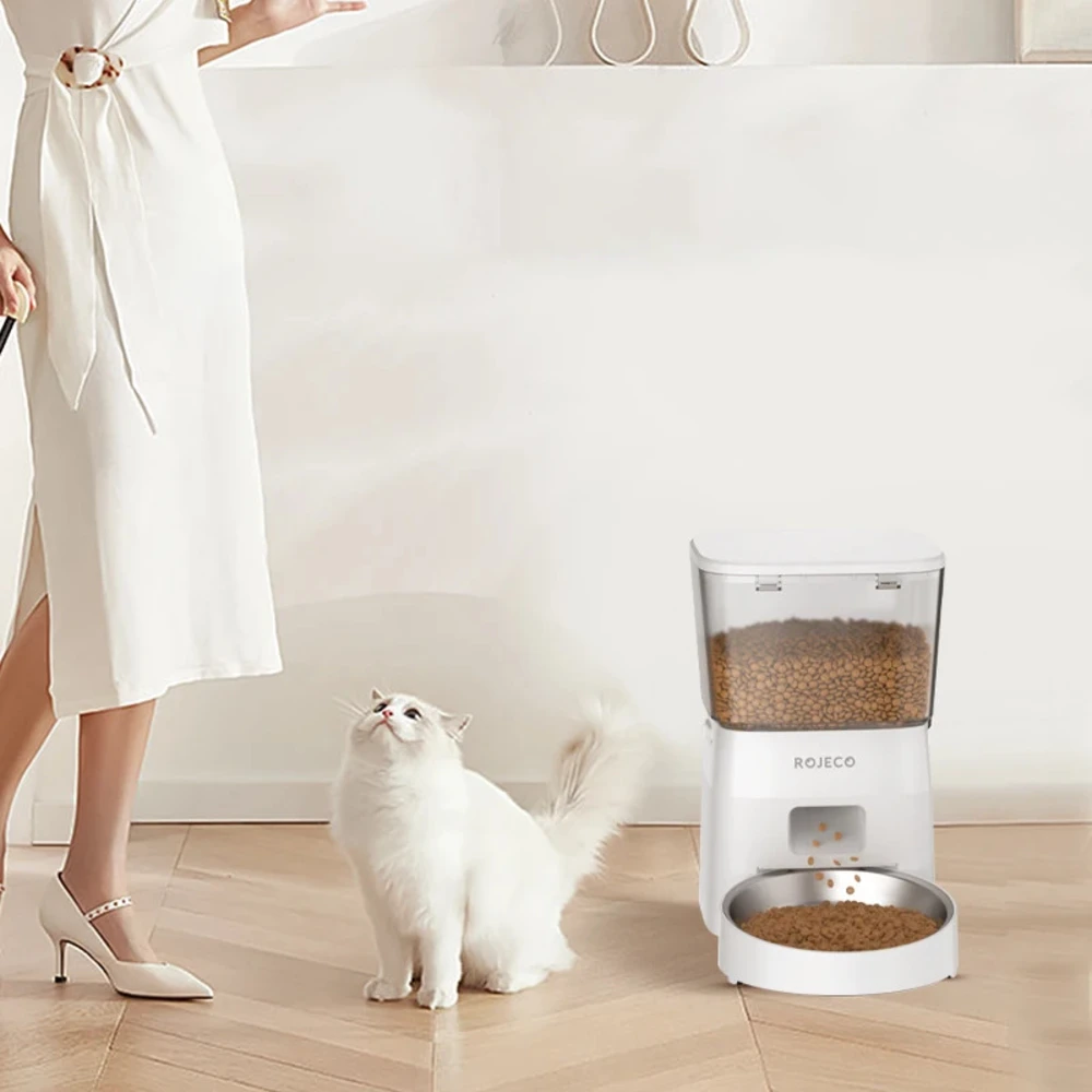 Femme en blanc debout près du distributeur Rojeco pendant que son chat regarde la gamelle